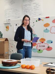 Janina Grosch von der FAU steht in einem Seminarraum. Sie hält ein kleines Buch in den Händen und spricht zu Personen außerhalb des Bildes.