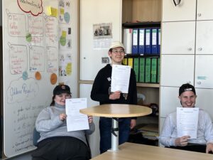 Drei Bildungsfachkräfte halten ihre Zwischenzeugnisse hoch.