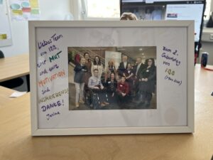 Ein Erinnerungsfoto in einem weißen Rahmen. Zehn Personen sind auf dem Foto abgebildet. Neben dem Bild steht eine Widmung.
