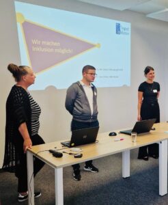 Zwei Frauen und ein Mann halten einen Vortrag. Sie sind von Input Inklusiv aus München.